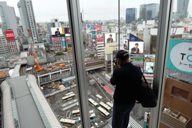 رجل يلتقط صورة لمنطقة شيبويا من منصة مراقبة في طوكيو (أ.ب)