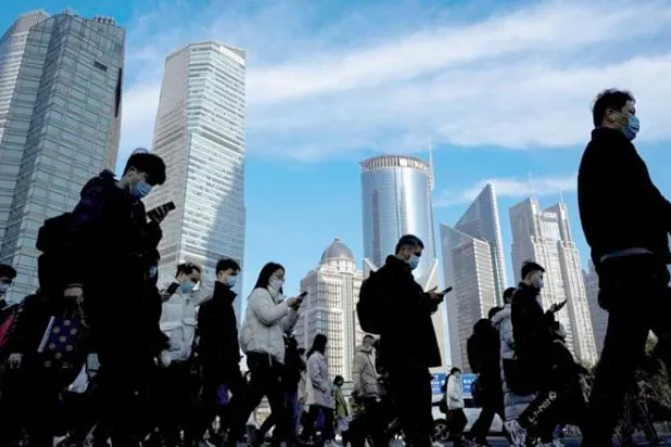 مشاة يعبرون الطريق في المنطقة المالية بمدينة شنغهاي الصينية (رويترز)