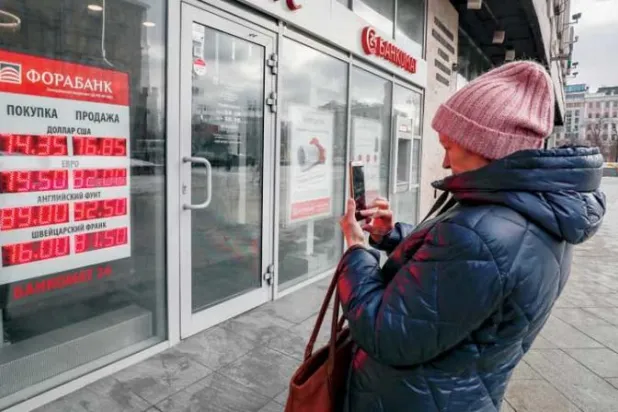 روسية تصور أحدث أسعار العملة المحلية مقابل نظيراتها الأجنبية على واجهة محل صيرفة بموسكو (إ.ب.أ)