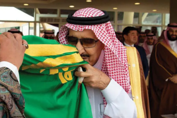 الملك سلمان بن عبد العزيز يقبّل العلم السعودي في إحدى المناسبات (واس)