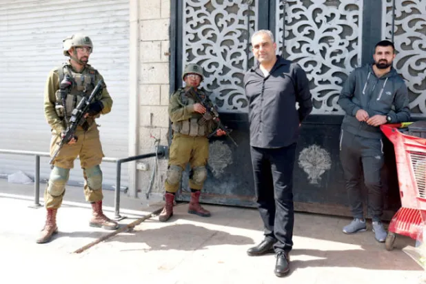 جنديان إسرائيليان أثناء منع فتح المتاجر الفلسطينية في حوارة الأربعاء الماضي في أعقاب هجوم الأحد (إ.ب.أ)