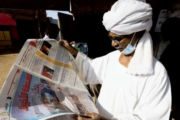 سوداني يقرأ جريدة محلية في مدينة أم درمان (رويترز)