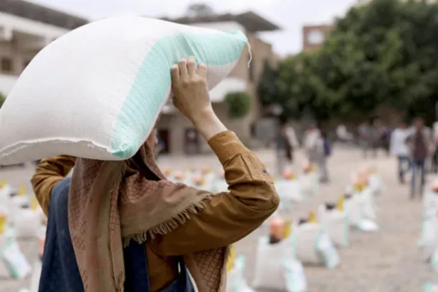 عامل في صنعاء يحمل كيساً من دقيق القمح خلال توزيع مساعدات غذائية من قبل جمعية خيرية محلية (رويترز)