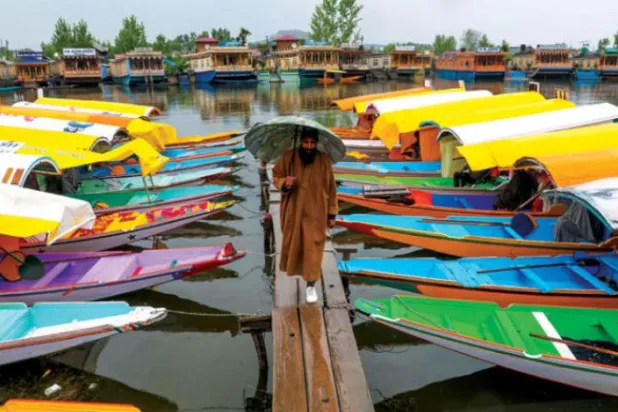 ایک ہندوستانی کشمیر میں سری نگر کی جھیل میں کشتیوں کے درمیان پل پر چل رہا ہے (ای پی اے)
