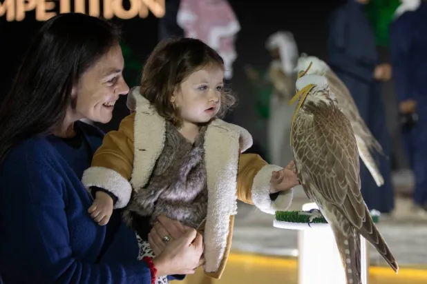 طفلة ووالدتها تداعبان صقراً خلال كأس العُلا للصقور (نادي الصقور)