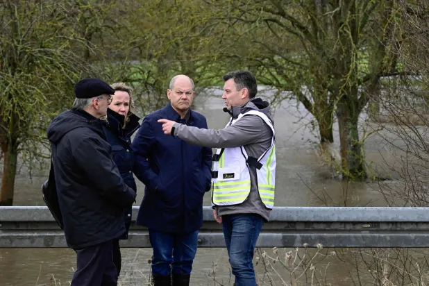 المستشار الألماني أولاف شولتس يستمع إلى المسؤولين وهم يقفون بجوار نهر هيلمه الفائض بشرق ألمانيا (أ.ف.ب)