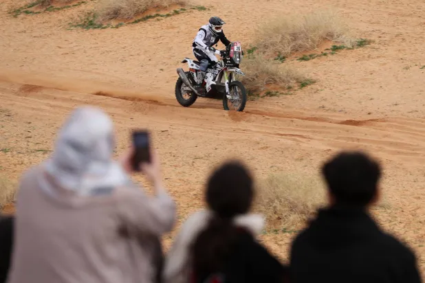 مجموعة عشاق للرالي يصورون دراجة نارية خلال منافسات الرالي (رويترز)