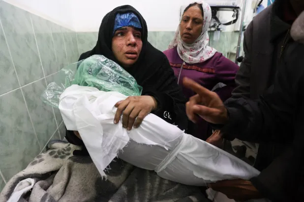 فلسطينية في مستشفى أبو يوسف النجار برفح وهي تحمل جثمان ابنتها التي قُتلت بغارة إسرائيلية اليوم السبت (رويترز)