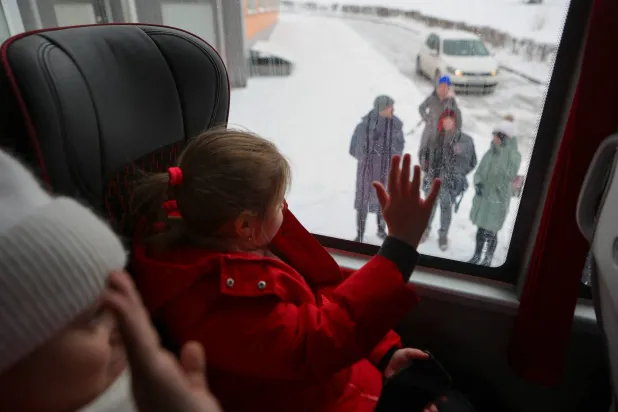 أطفال يلوّحون لآبائهم أثناء مغادرتهم بالحافلة إلى معسكرات الترفيه في منطقة فورونيج المجاورة نتيجة القصف الأوكراني في بيلغورود (رويترز)