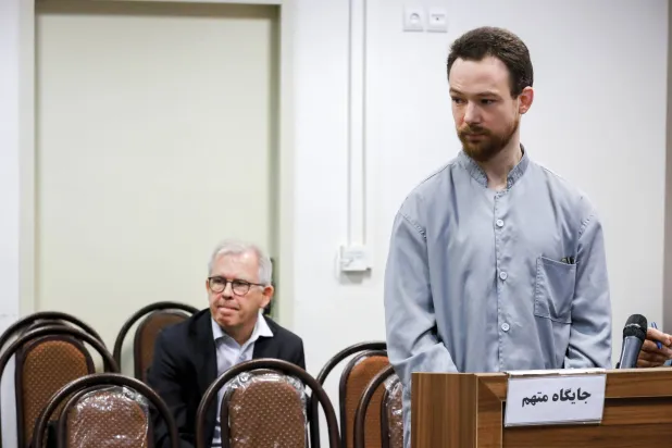 المواطن السويدي يوهان فلوديروس يقف أمام الوزير المستشار ورئيس بعثة سفارة السويد بطهران لارس روناس ويجلس في قاعة المحكمة الثورية بطهران في إيران (أ.ب)