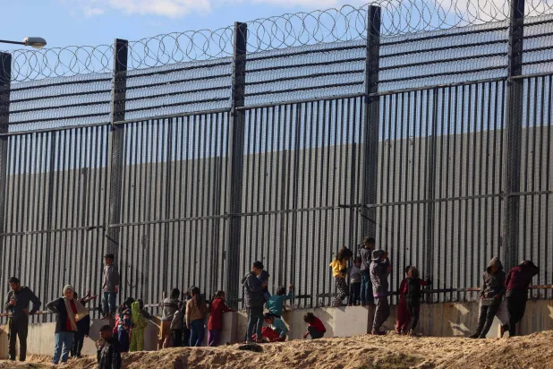 فلسطينيون بجانب السياج الحدودي مع مصر في مخيم مؤقت للنازحين في رفح جنوب قطاع غزة الأربعاء (أ.ف.ب)