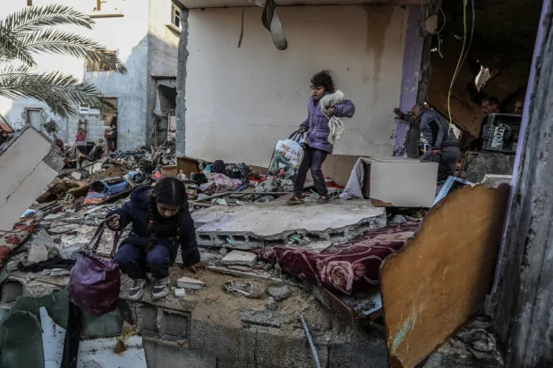 طفلتان تحملان أغراضهما وسط منزل دمرته غارة إسرائيلية في رفح السبت (د.ب.أ)