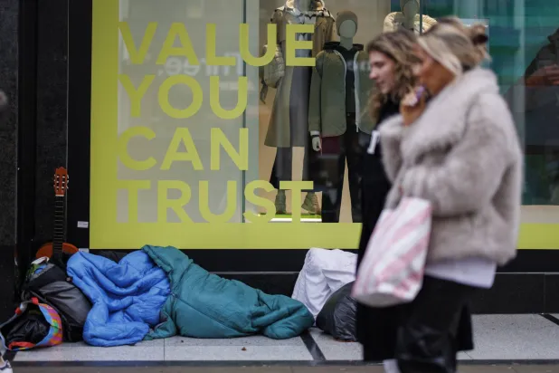 سيدتان تمران قرب مشرّد نائم في شارع أكسفورد ستريت التجاري في قلب لندن (إ.ب.أ)