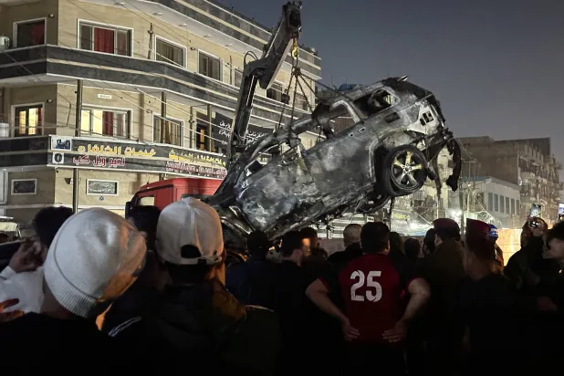 رفع سيارة محطمة على شاحنة بعد استهدافها بطائرة مسيرة في بغداد (رويترز)