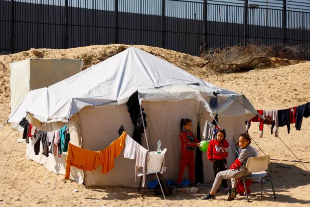 أطفال يتجمعون بالقرب من خيمة في رفح على الحدود مع مصر (رويترز)