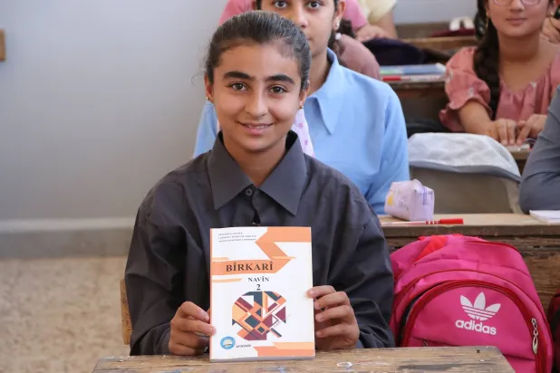 الطالبة مزكين دلو تمسك كتاب الرياضيات بعد ترجمته إلى لغتها الأم الكردية (الشرق الأوسط)