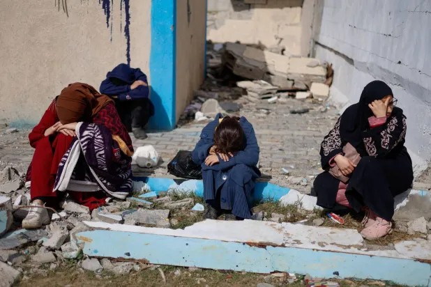 فلسطينيون يجلسون بجوار مبان مدمرة في رفح نتيجة القصف الإسرائيلي (رويترز)