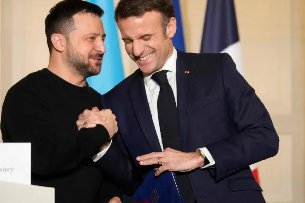 Emmanuel Macron ve Vladimir Zelensky ortak güvenlik anlaşmasını imzaladıktan sonra sıcak bir şekilde el sıkışıyor (AFP)