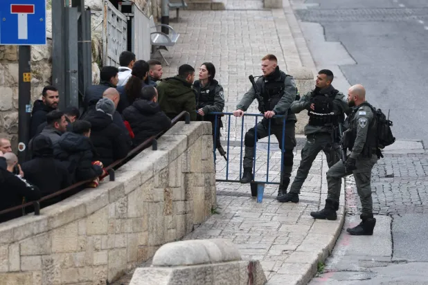 أحد أفراد قوات الأمن الإسرائيلية يتحدث إلى المصلين بينما ينتظر الناس عند نقطة تفتيش بالقرب من باب الأسباط لدخول مجمع المسجد الأقصى قبل صلاة الجمعة الماضية (أ.ف.ب)