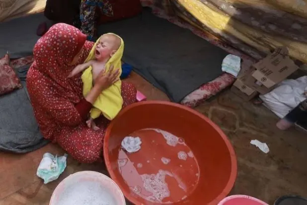 امرأة نازحة تغسل رضيعاً داخل إحدى الخيم في رفح وسط الحرب المستمرة منذ السابع من أكتوبر (أ.ف.ب)