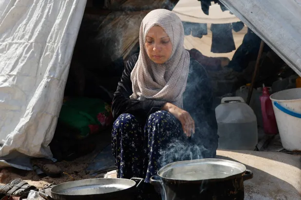 سيدة فلسطينية تطهو الطعام أمام خيمتها في رفح جنوب غزة (رويترز)
