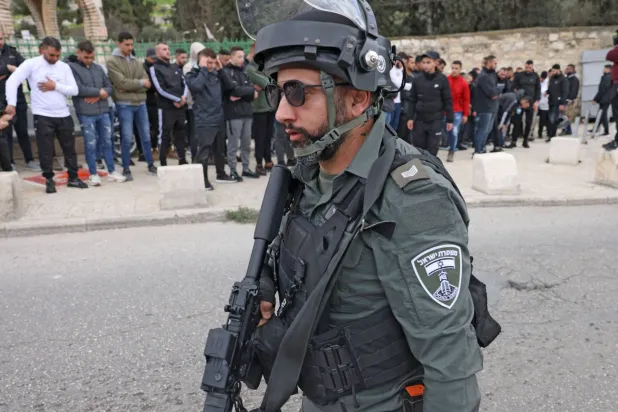 رجل أمن إسرائيلي قرب فلسطينيين يؤدون صلاة الجمعة في شارع بالقدس الشرقية (أ.ف.ب)
