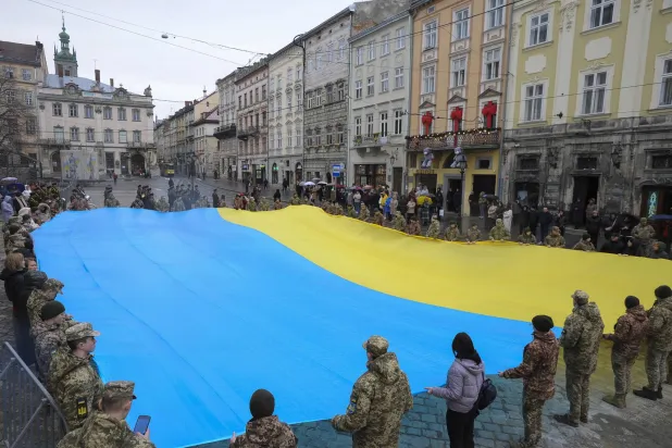 طلاب عسكريون ومدنيون يحملون علماً وطنياً أوكرانياً كبيراً أثناء غناء النشيد الوطني الأوكراني في لفيف بغرب أوكرانيا في 11 مارس 2024 وسط الغزو الروسي للبلاد (إ.ب.أ)