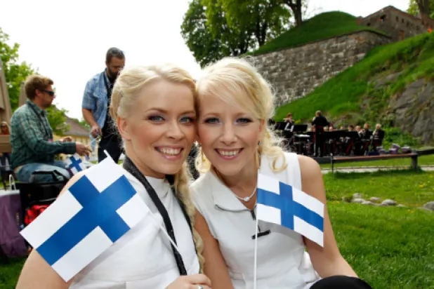 فنلنديون خلال احتفال وفي وسط الصورة فتاتان تبتسمان وتحملان علم فنلندا (متداولة)