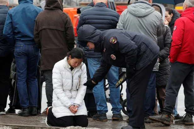 شرطيّ روسي يقترب من سيدة يبدو عليها التأثر خارج قاعة الحفلات الموسيقية التي شهدت هجوماً دموياً في موسكو (رويترز)
