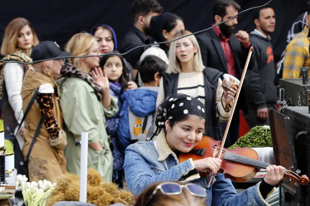 أشخاص يجتمعون حول فتاة إيرانية تعزف على الكمان في سوق تجريش شمال طهران عشية عيد النورزو الأسبوع الماضي (إ.ب.أ)
