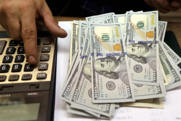 رجل يضرب على ألة حاسبة بجوار فئات نقدية من الدولار (رويترز)