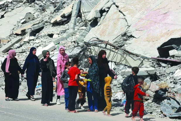 
نساء وأطفال يمشون بجوار مبنى دمره القصف الإسرائيلي في رفح جنوب قطاع غزة أمس (أ.ف.ب)