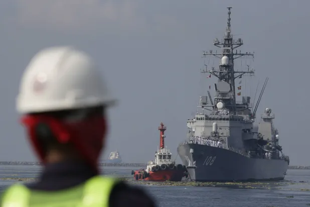 عامل ميناء فلبيني ينظر إلى مدمرة يابانية تستعد للرسو في الميناء الجنوبي لمانيلا للمشاركة في المناورة البحرية المشتركة (أ.ب)