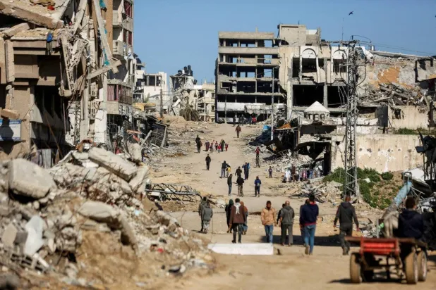 Gazze'de İsrail bombardımanı sırasında yıkılan evlerin yakınında yürüyen Filistinliler (Reuters)