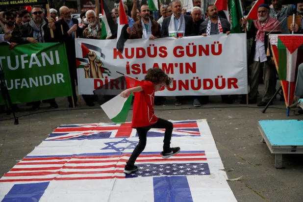 طفل يدوس على أعلام الولايات المتحدة والمملكة المتحدة وإسرائيل في «يوم القدس» بإسطنبول يوم 5 أبريل الحالي (رويترز)