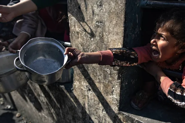 طفلة فلسطينية نازحة تحمل وعاءً فارغاً وتنتظر مع آخرين المساعدات الغذائية في مخيم رفح للاجئين جنوب قطاع غزة في 25 يناير (إ.ب.أ)