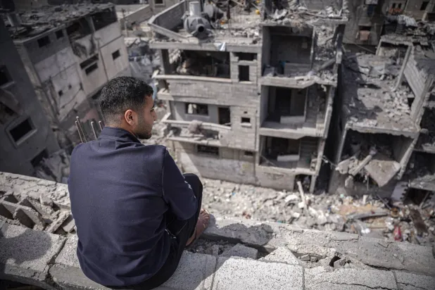 شاب فلسطيني يجلس فوق منزله المدمر بسبب القصف الإسرائيلي على وسط قطاع غزة (د.ب.أ)