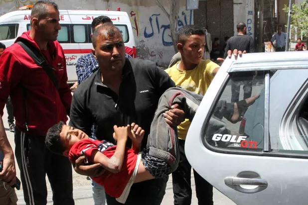 فلسطيني يحمل صبياً أُصيب في غارة إسرائيلية على رفح بجنوب قطاع غزة (رويترز)