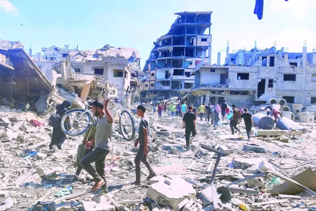 İsrail ordusunun dün Gazze'nin Zeytun Mahallesi’nden çekilmesinin ardından İsrail hava saldırılarında yıkılan binaların enkazı arasında yürüyen Filistinliler (DPA)