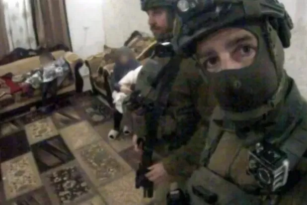 صورة التُقطت من أحد مقاطع الفيديو التي نشرها يوهاي فازانا تظهر أفراد كتيبته وهم يدخلون بالقوة أحد المنازل ويقفون أمام امرأة فلسطينية مع طفل (حسابه على فيسبوك - بي بي سي)