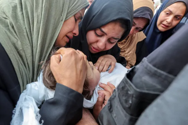 أم فلسطينية وأقاربها يوم الأحد في دير البلح يحملون جثمان طفلة قتلتها غارة إسرائيلية (رويترز)