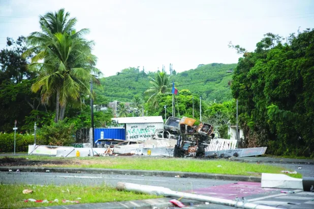 Kaledonya'nın başkenti Nouméa'nın bir banliyösünün girişinde yanmış arabalar ve barikatlar (AFP)
