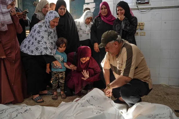 فلسطينيون يتجمعون حول جثث أثناء التعرف على الضحايا في مستشفى «شهداء الأقصى» في دير البلح بعد القصف الإسرائيلي (أ.ف.ب)