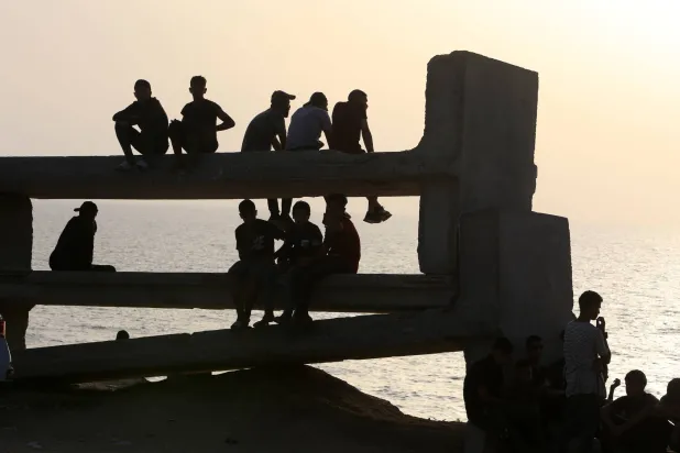 فلسطينيون يجلسون قرب الرصيف البحري العائم في انتظار وصول المساعدات الإنسانية لغزة (د.ب.أ)