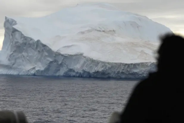 أحد الركاب على متن سفينة بحرية تشيلية ينظر إلى جبل جليدي في القارة القطبية الجنوبية (أ.ب)