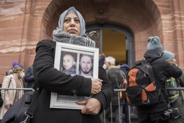 ياسمين المشعان عضو رابطة عائلات قيصر تحمل صور ضحايا النظام السوري أمام محكمة  ألمانية 13 يناير 2022 (أ.ف.ب)