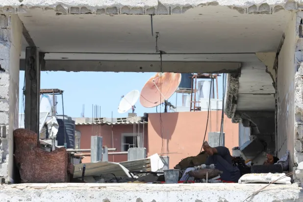 شخص يستلقي بمبنى تضرر في الهجوم العسكري الإسرائيلي في خان يونس جنوب قطاع غزة الخميس (رويترز)