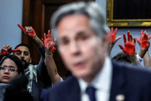 متظاهرون مؤيدون للفلسطينيين يرفعون الأيادي الحمراء بينما يدلي وزير الخارجية الأميركي أنتوني بلينكن بشهادته أمام جلسة استماع في «كابيتول هيل» بواشنطن يوم 22 مايو 2024 (رويترز)