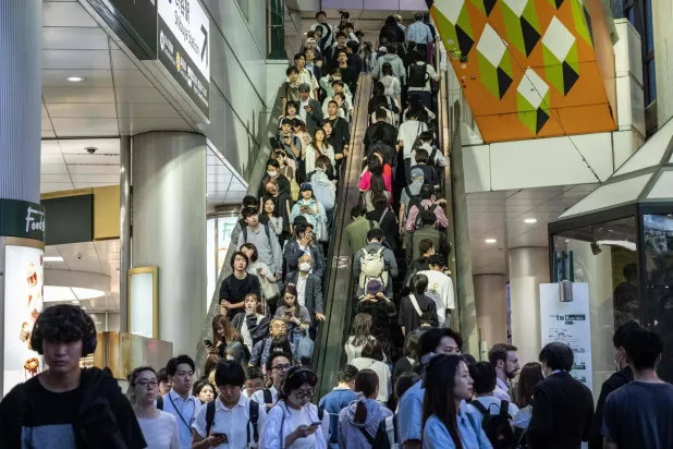 أشخاص يستقلون سلماً كهربائياً في محطة شيبويا في طوكيو (أ.ف.ب)