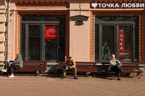 أشخاص يستريحون على مقاعد بالقرب من نافذة مبنى تجاري معروض للإيجار في موسكو (رويترز)